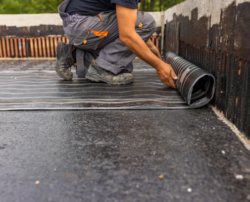 Worker laying the vapor barrier for the roof, bituminous membrane to be welded with flame