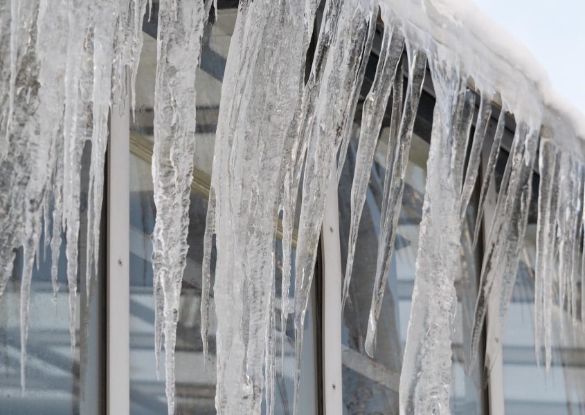 Icicles hang from roof and wall in winter frozen