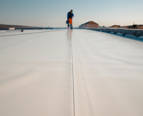 Worker on a replaced white commercial roof under a clear sky.