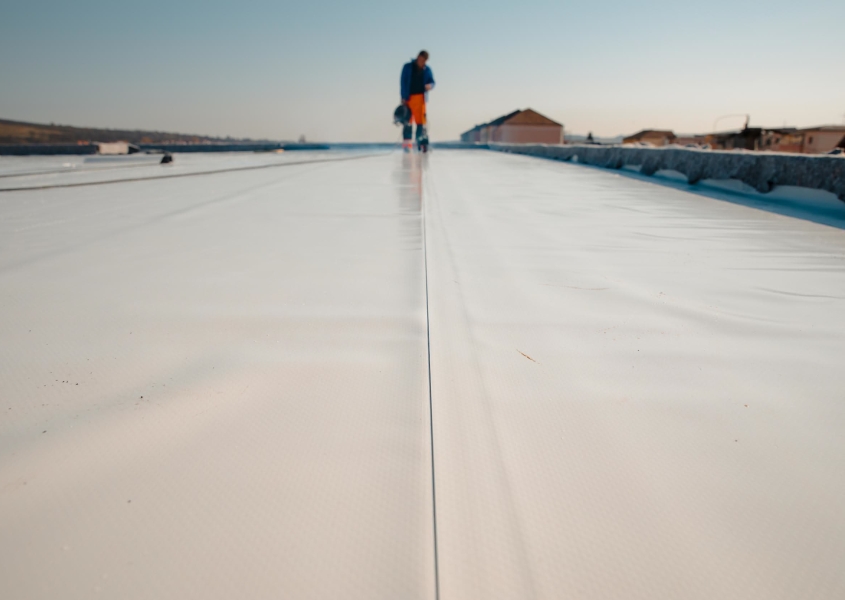 Worker on a replaced white commercial roof under a clear sky.