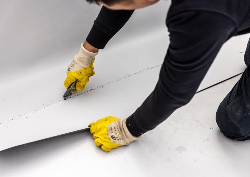 A roofer conducting preventative roof maintenance on a commercial building's flat roof.