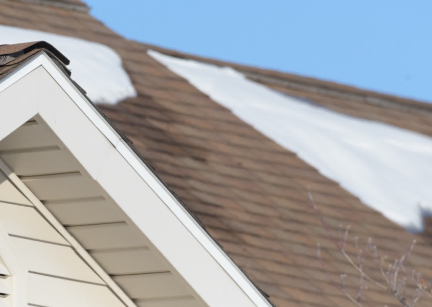 Roofer removing snow from residential roof in Wisconsin winter
