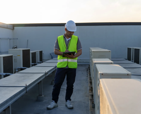 Roofer inspecting a commercial flat roof for drainage problems near HVAC units