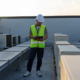 Roofer inspecting a commercial flat roof for drainage problems near HVAC units